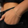 Close-up of a 3mm 14K gold color moissanite tennis bracelet on a woman’s wrist with hip hop streetwear styling.