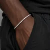 Close-up of a 3mm 14K gold color moissanite tennis bracelet on a woman’s wrist with hip hop streetwear styling.